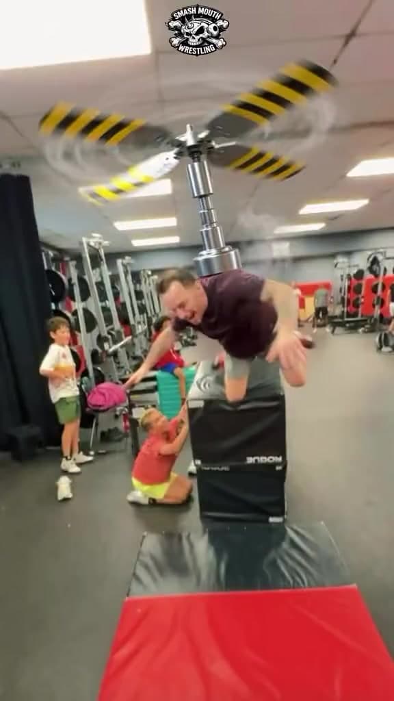 Smash Mouth Wrestling coach mid-air on a box-jump stunt at youth practice